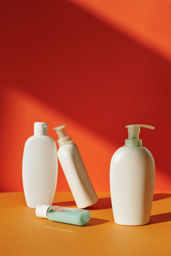 Services Plastic skincare bottles against a bright orange backdrop creating a minimalist aesthetic.