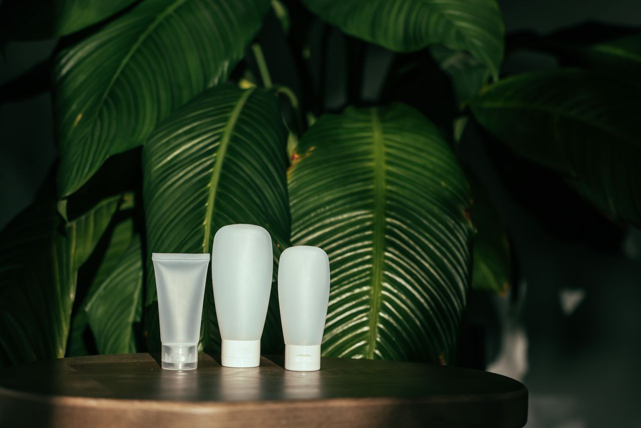 Contact White cosmetic containers with green leaves backdrop, perfect for eco-friendly product representation.